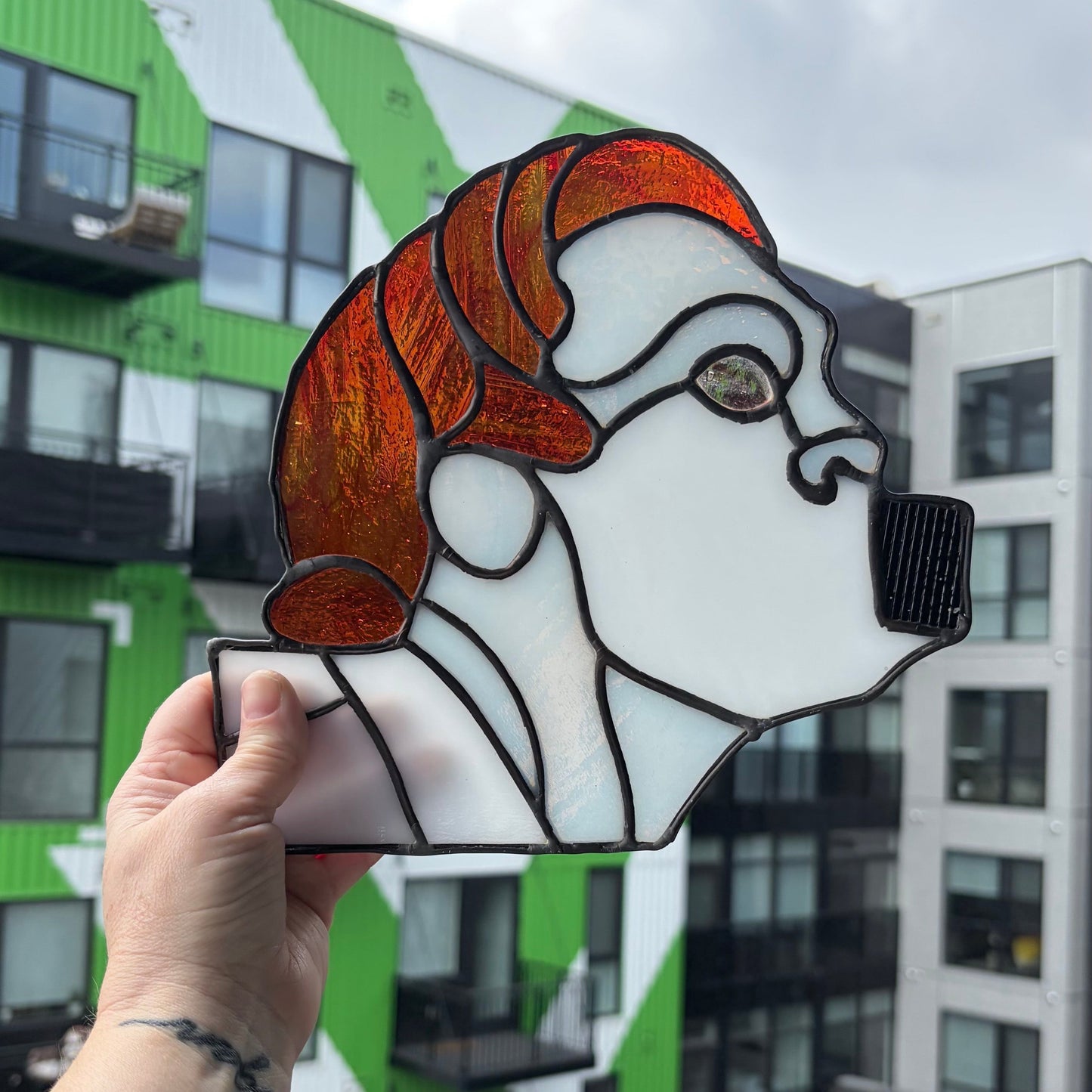 Person holding a stained glass window panel of a face with buildings in the background